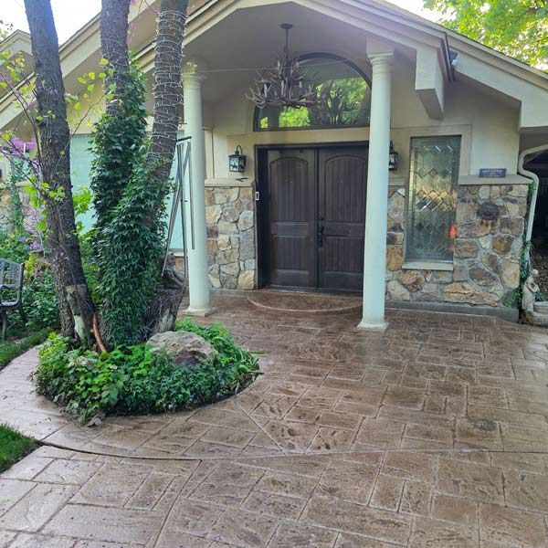 Stone-front house entry with double wooden doors, white columns, and a wet stamped-concrete walkway