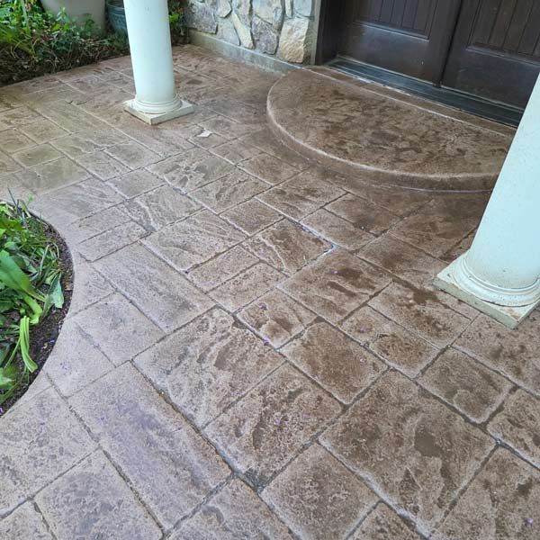 Wet stamped concrete porch with two white columns and a dark front door