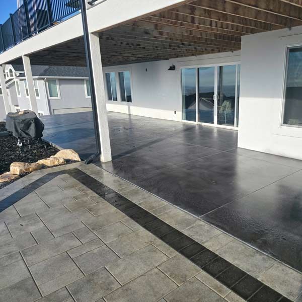 Covered patio with dark tile flooring, sliding glass doors, and a small grill area beside a house.
