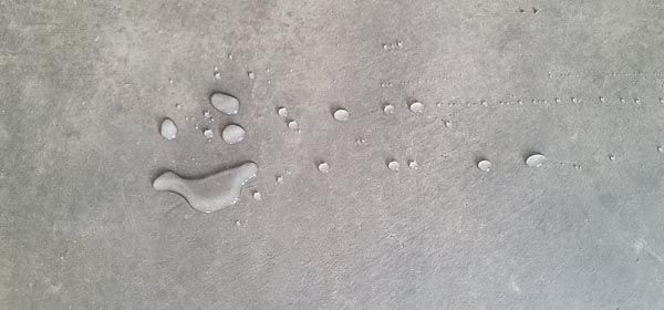 Small water puddle on gray concrete with scattered droplets and a footprint-like shape