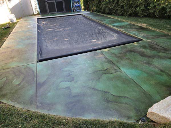 Backyard pool area with a covered rectangular pool and green-tinted concrete deck.