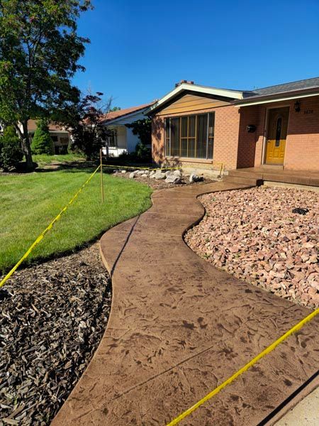 Curved concrete walkway through a front yard to a house with green lawn and mulch beds