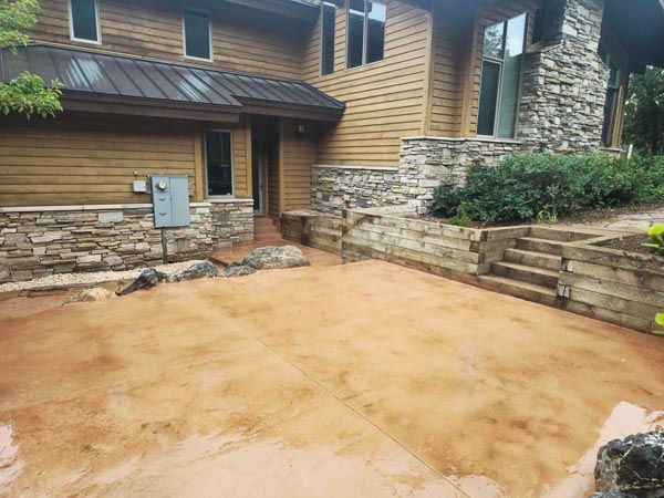 Empty dirt courtyard beside a rustic stone-and-wood house with steps and retaining walls