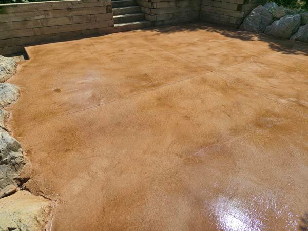 Wet sandy area in a small enclosed courtyard bordered by rocks and wooden walls