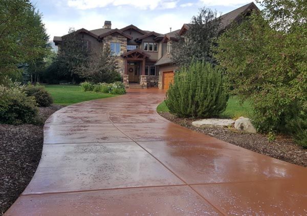 Winding wet driveway leading to a large house with trees and shrubs in front