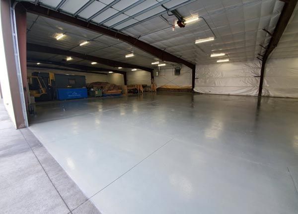Empty industrial warehouse with polished gray floor and metal roof, viewed from the entrance