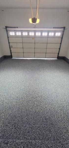 Empty garage with a closed white sectional door and speckled gray floor under a hanging light.