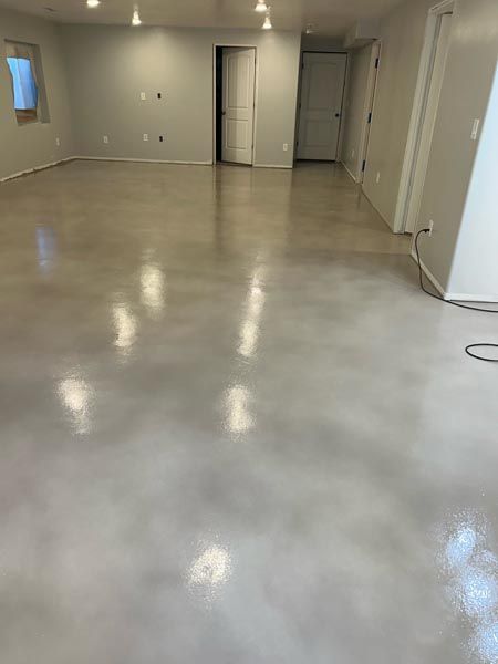 Empty unfinished room with glossy concrete floor, white walls, recessed lights, and open doorways.