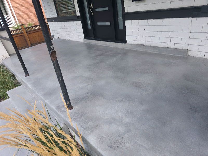 Concrete front porch with black door, white brick wall, and a rusted metal post.