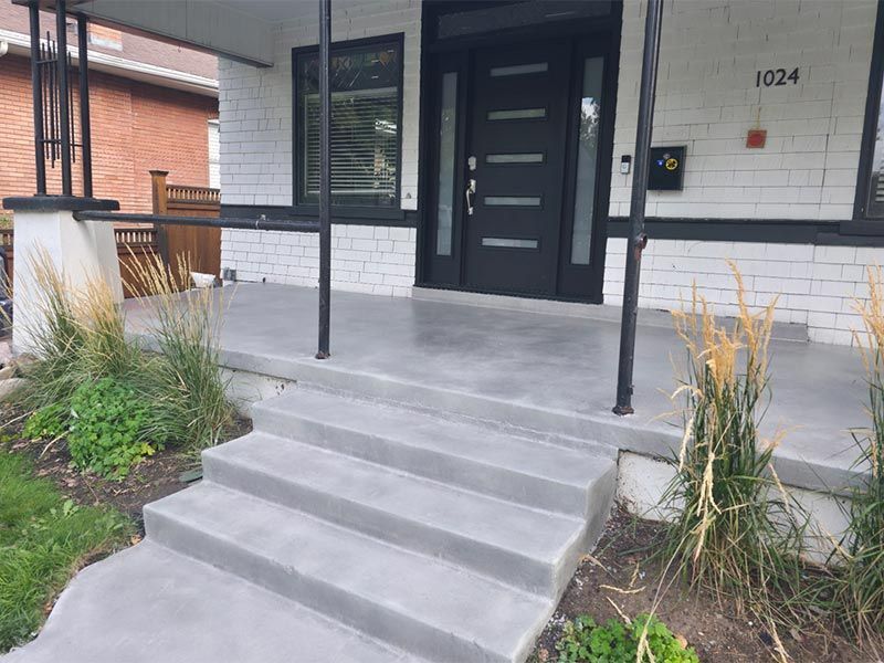 Front entrance with concrete steps, black door, and white brick facade framed by greenery