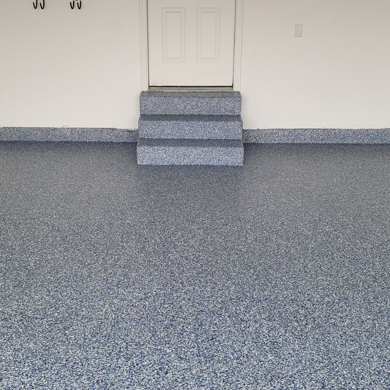 Empty garage with gray speckled floor and a small three-step stair leading to a closed door.