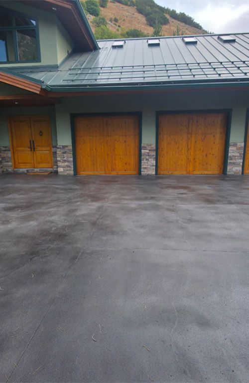 Three wooden garage doors under a sloped roof beside a dark paved driveway