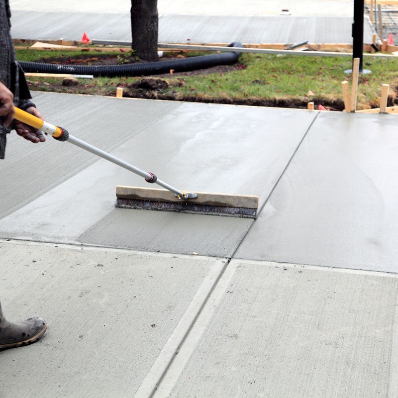 Worker smoothing wet concrete with a long-handled squeegee on a driveway slab