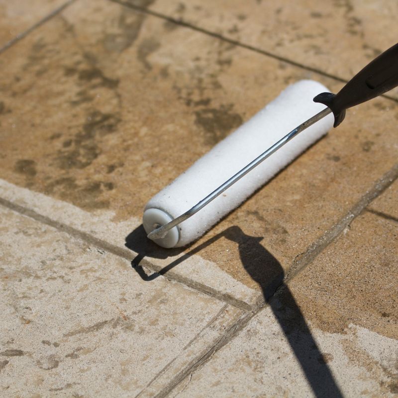 White paint roller on a tan tiled surface, with a dark handle and shadow.