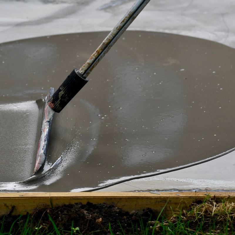Person smoothing wet gray cement with a trowel on a concrete slab