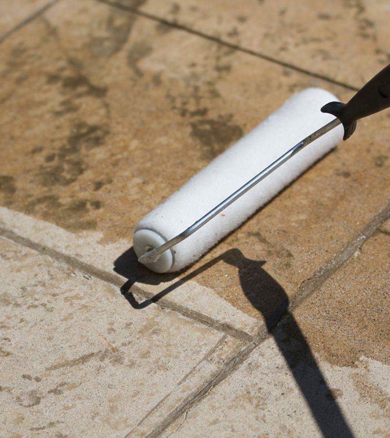 White paint roller on a concrete surface, casting a long shadow in sunlight