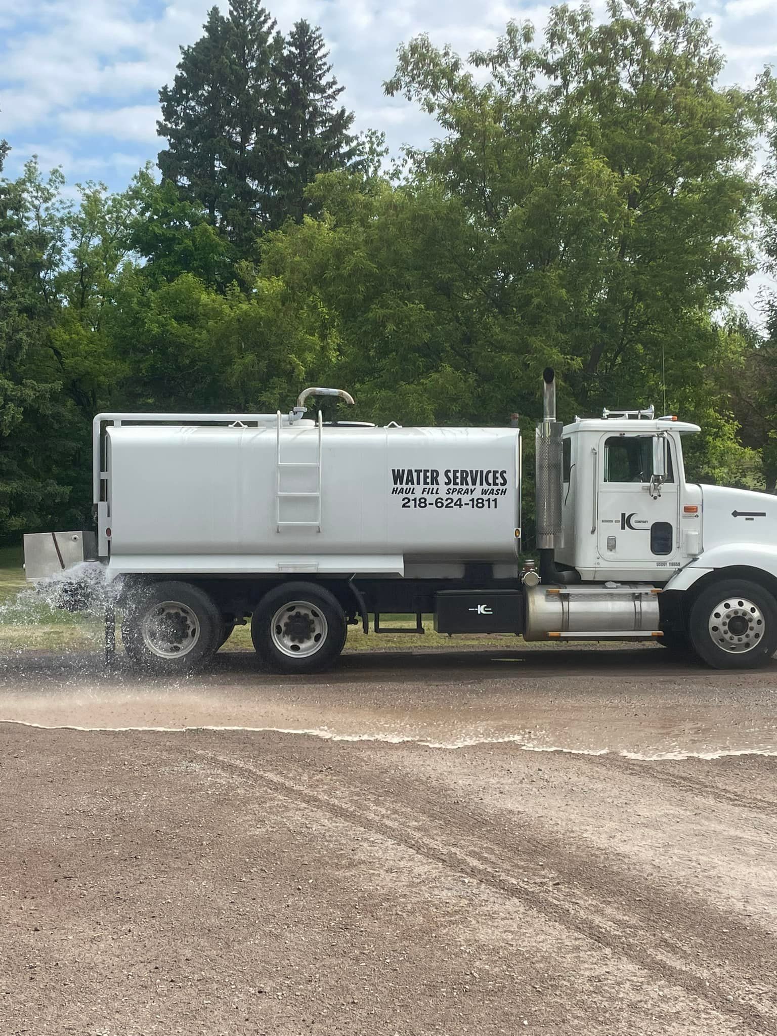 A white water truck is spraying water on a gravel road.