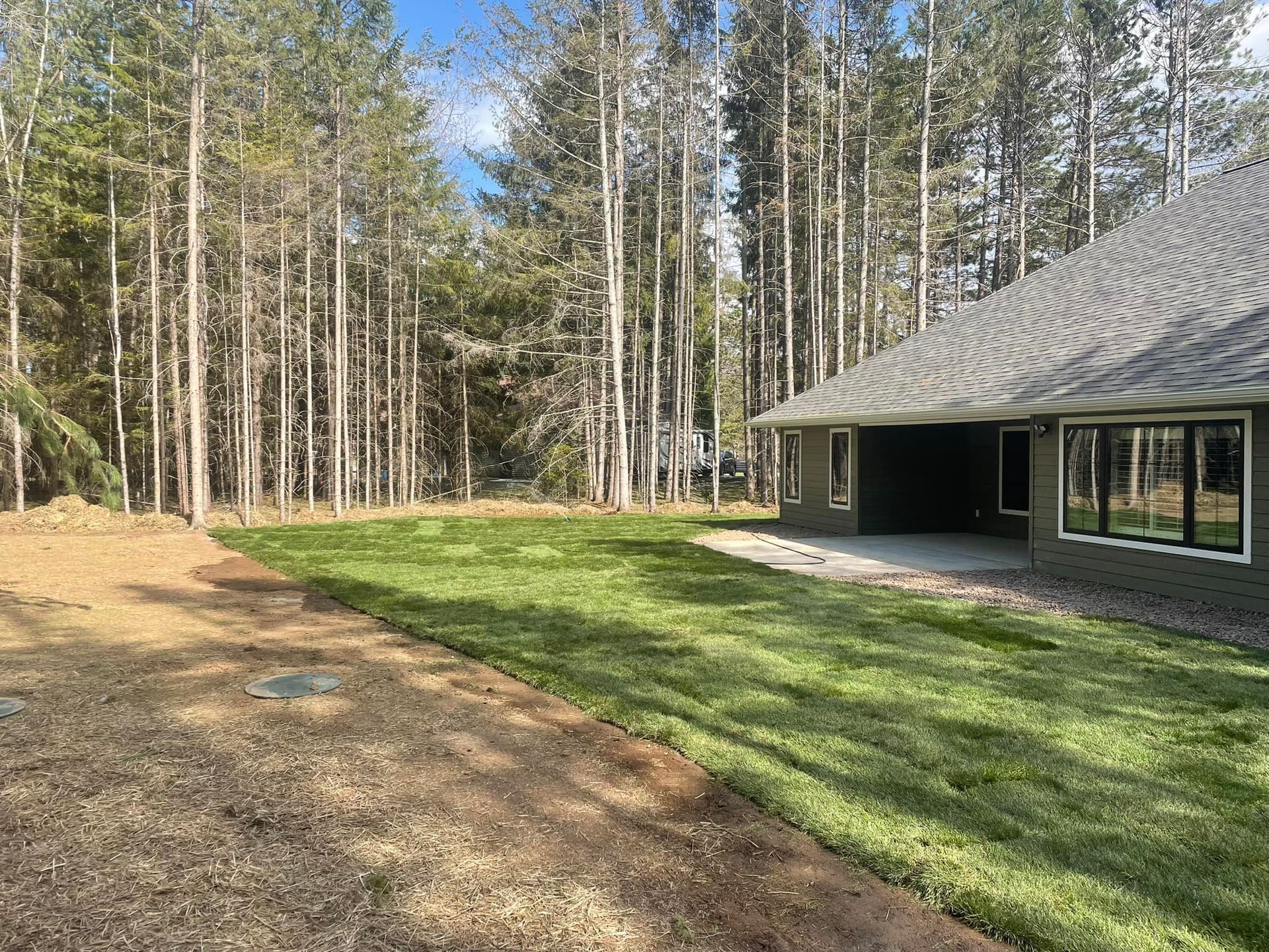 A house in the middle of a forest with a large lawn in front of it.