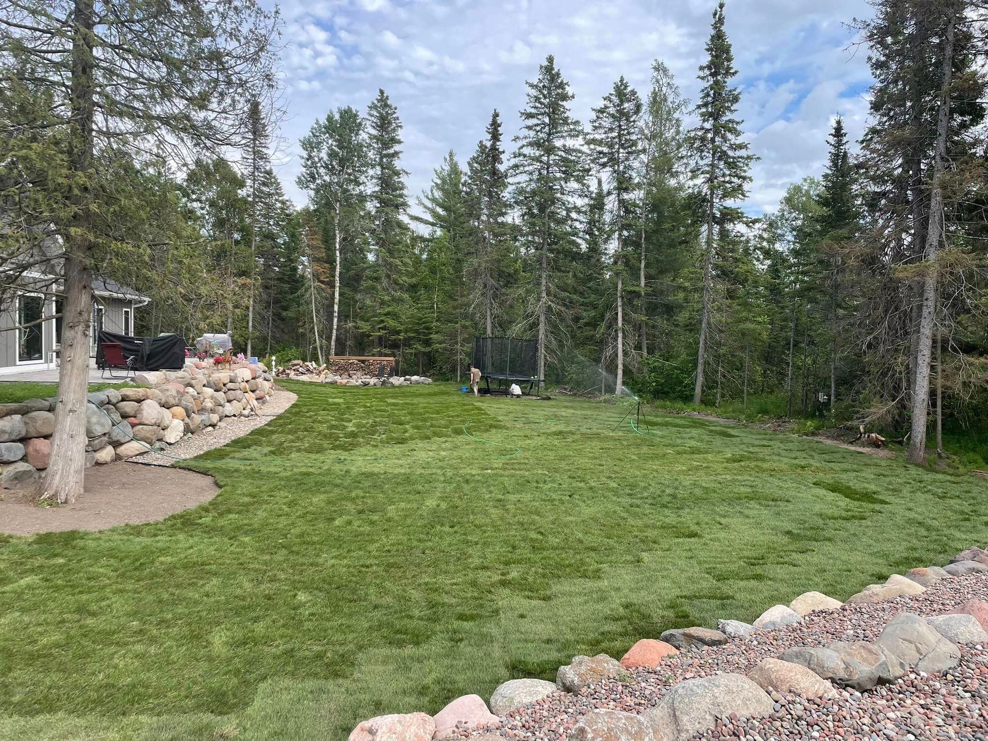 A large lush green field surrounded by trees and rocks.