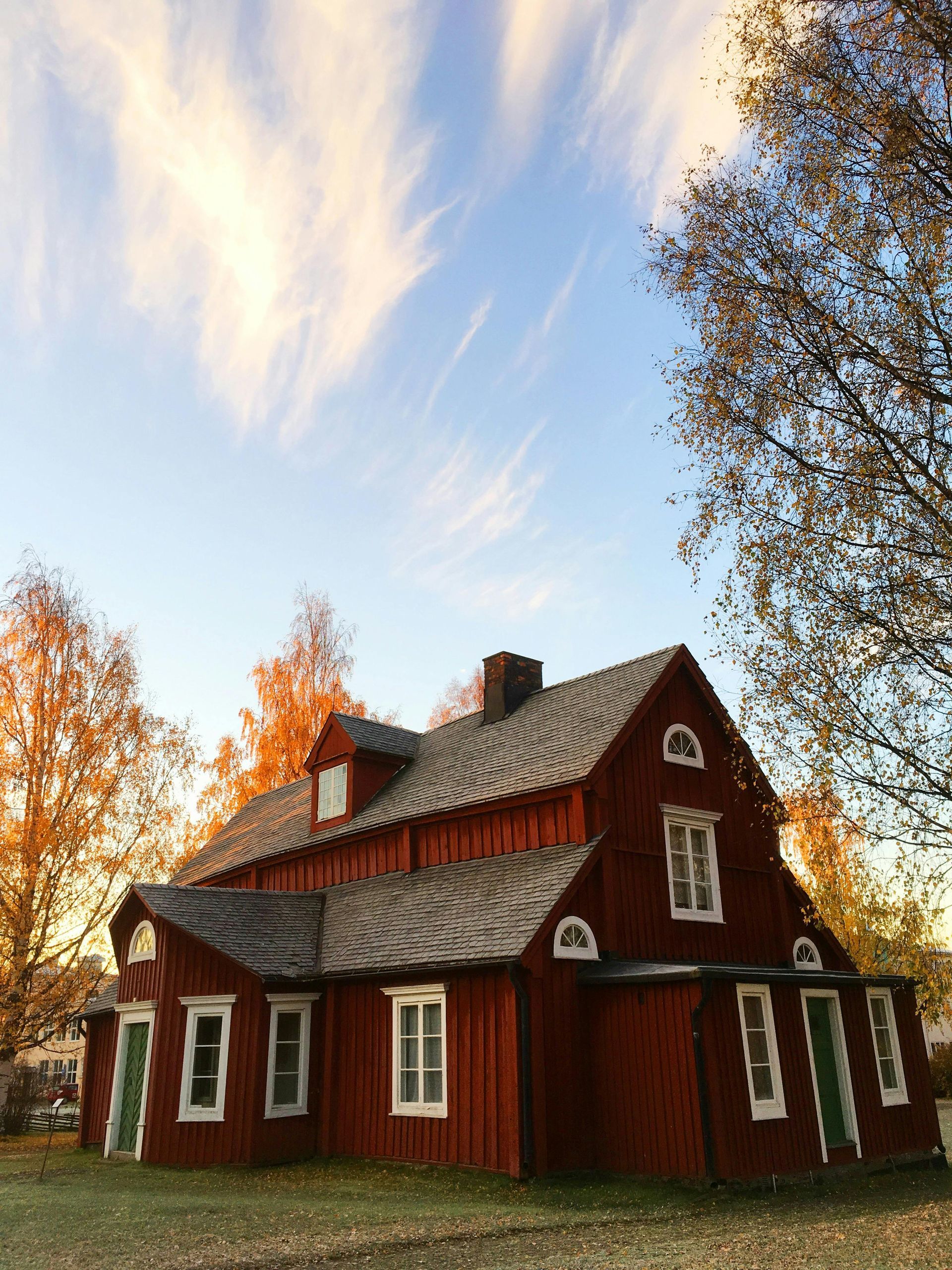 A red house with a wooden roof is surrounded by trees and a blue sky.