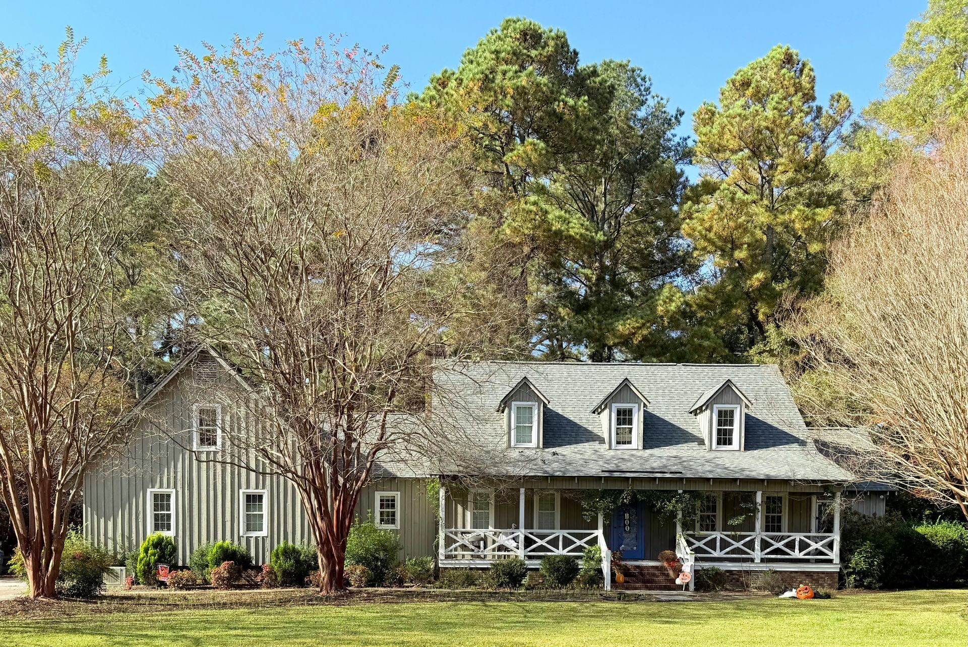 A large house with a large porch is surrounded by trees in a field.
