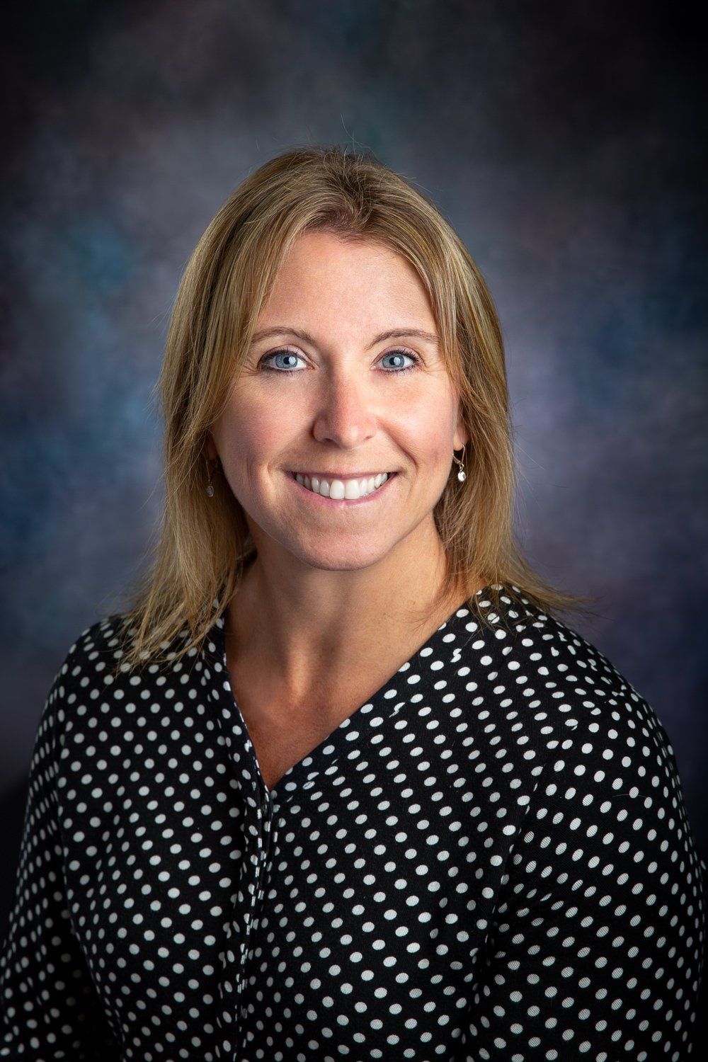 A woman in a black and white polka dot shirt is smiling for the camera.