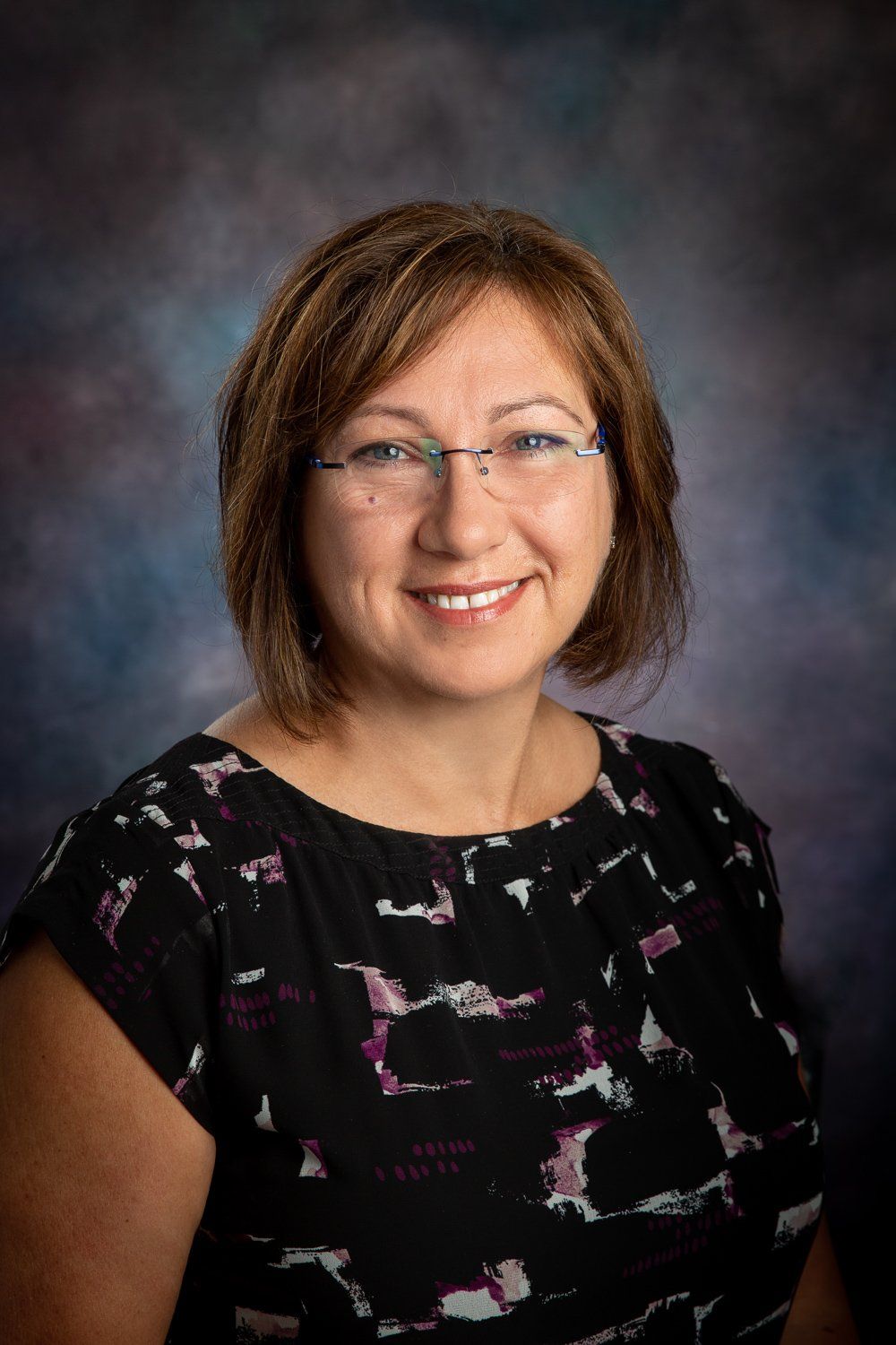 A woman wearing glasses and a black dress is smiling for the camera.
