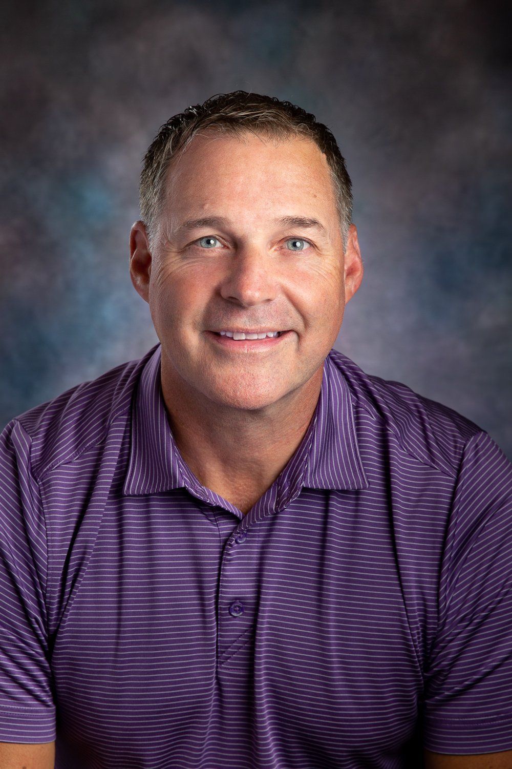A man in a purple shirt is smiling for the camera.