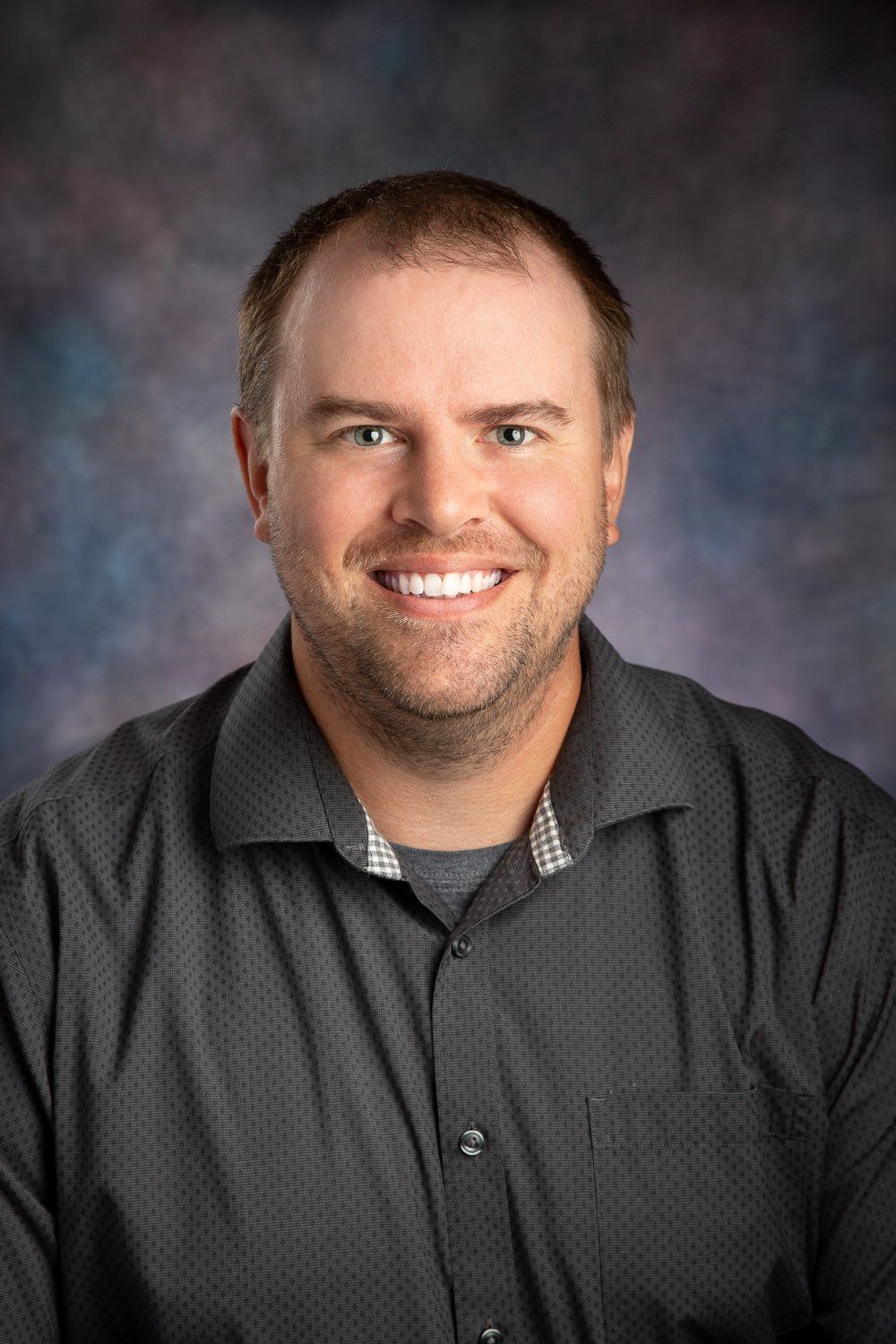 A man in a gray shirt is smiling for the camera.