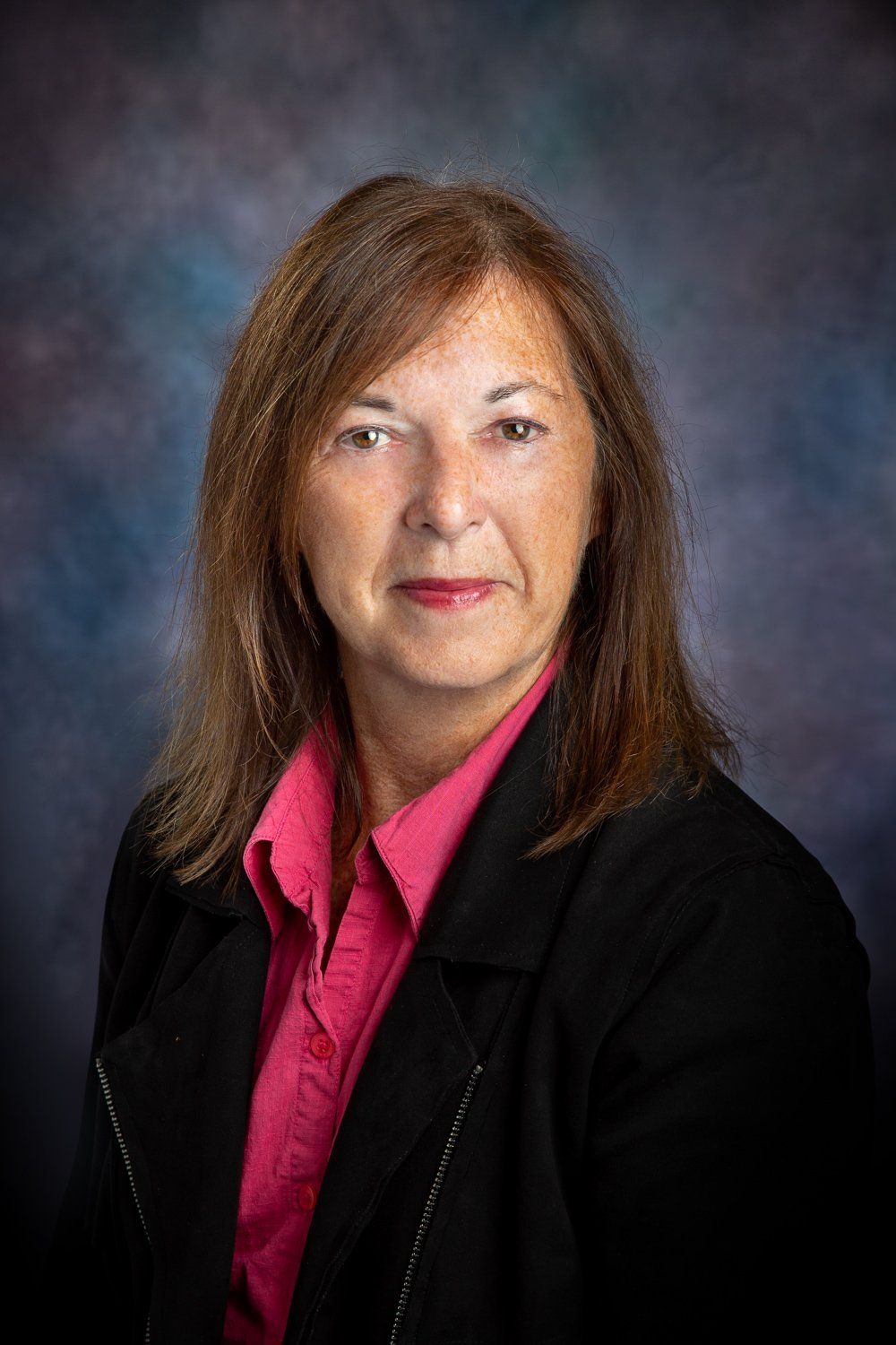 A woman in a pink shirt and black jacket is posing for a picture.