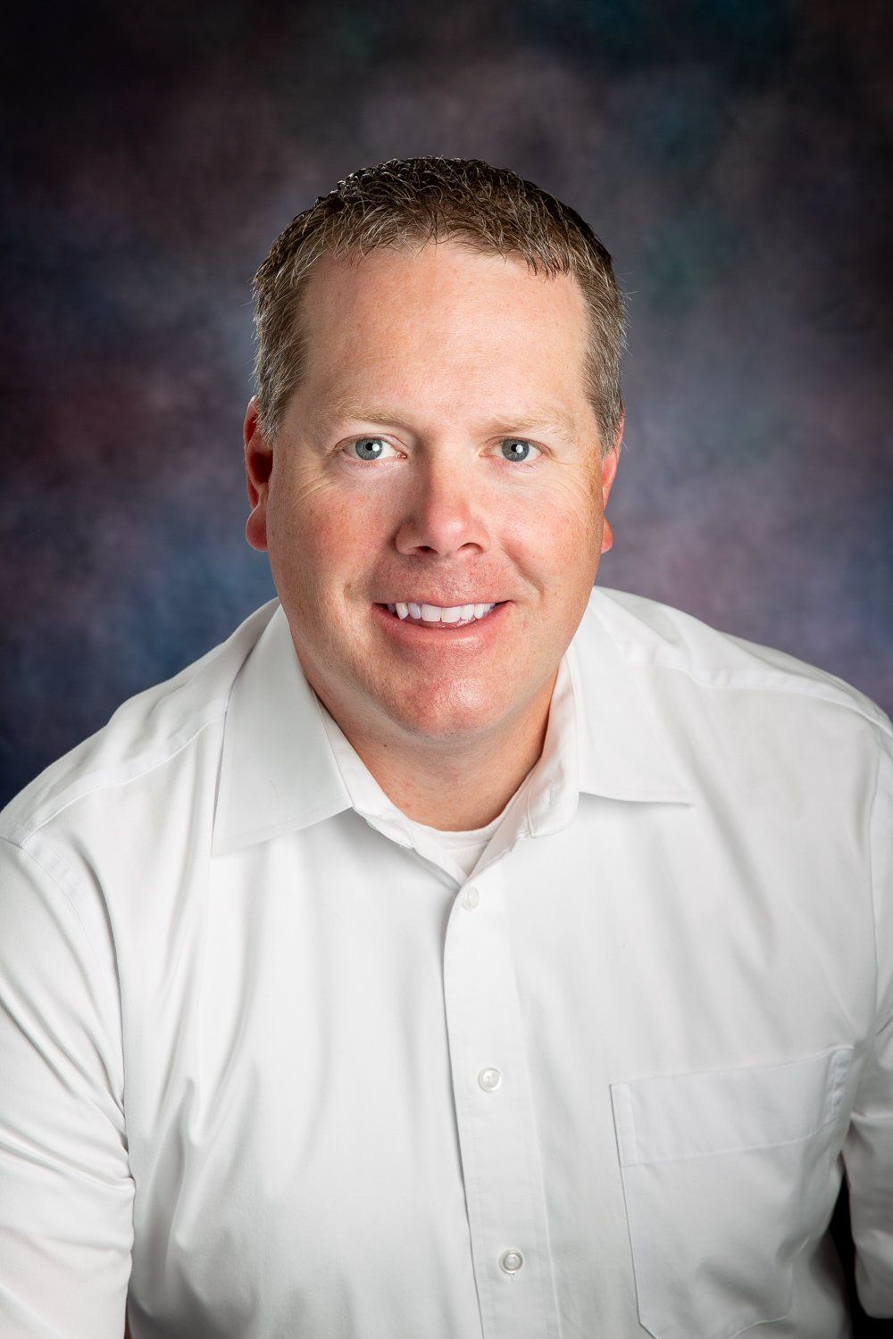 A man in a white shirt is smiling for the camera.