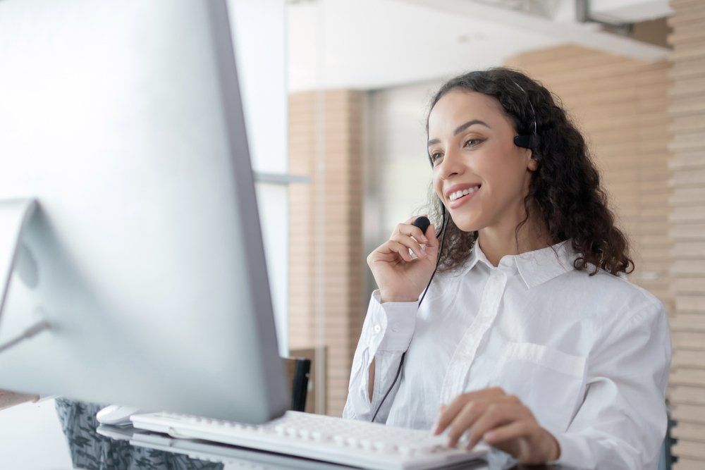 A woman wearing a headset is sitting in front of a computer.
