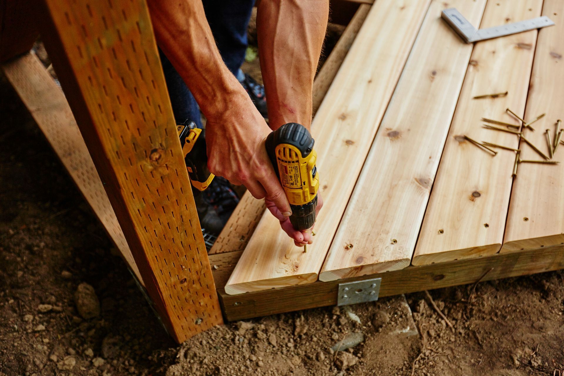 Person using a drill to secure wooden planks on a structure outdoors.