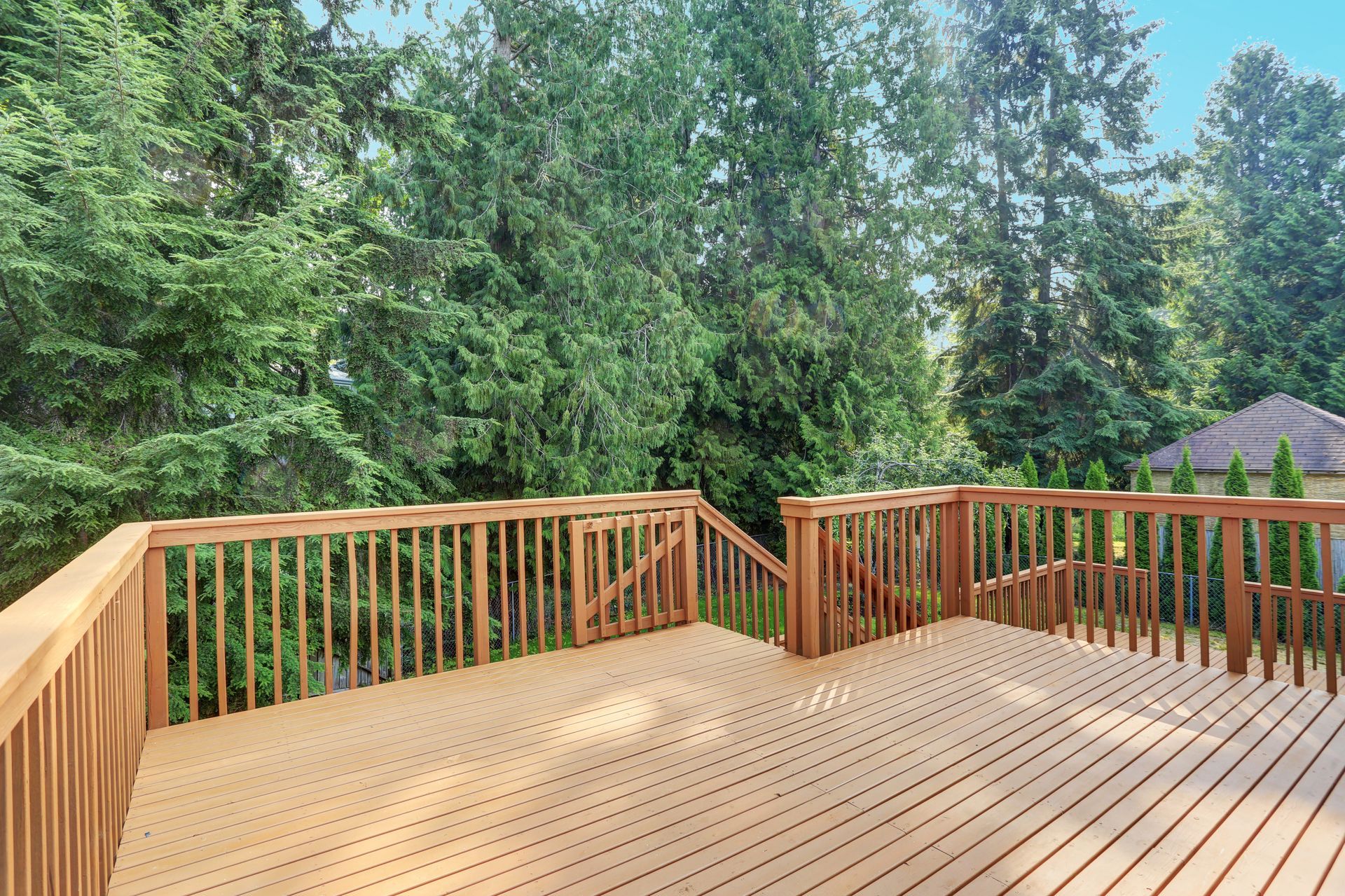 Wooden deck with railing, stairs, and lush green trees in the background.