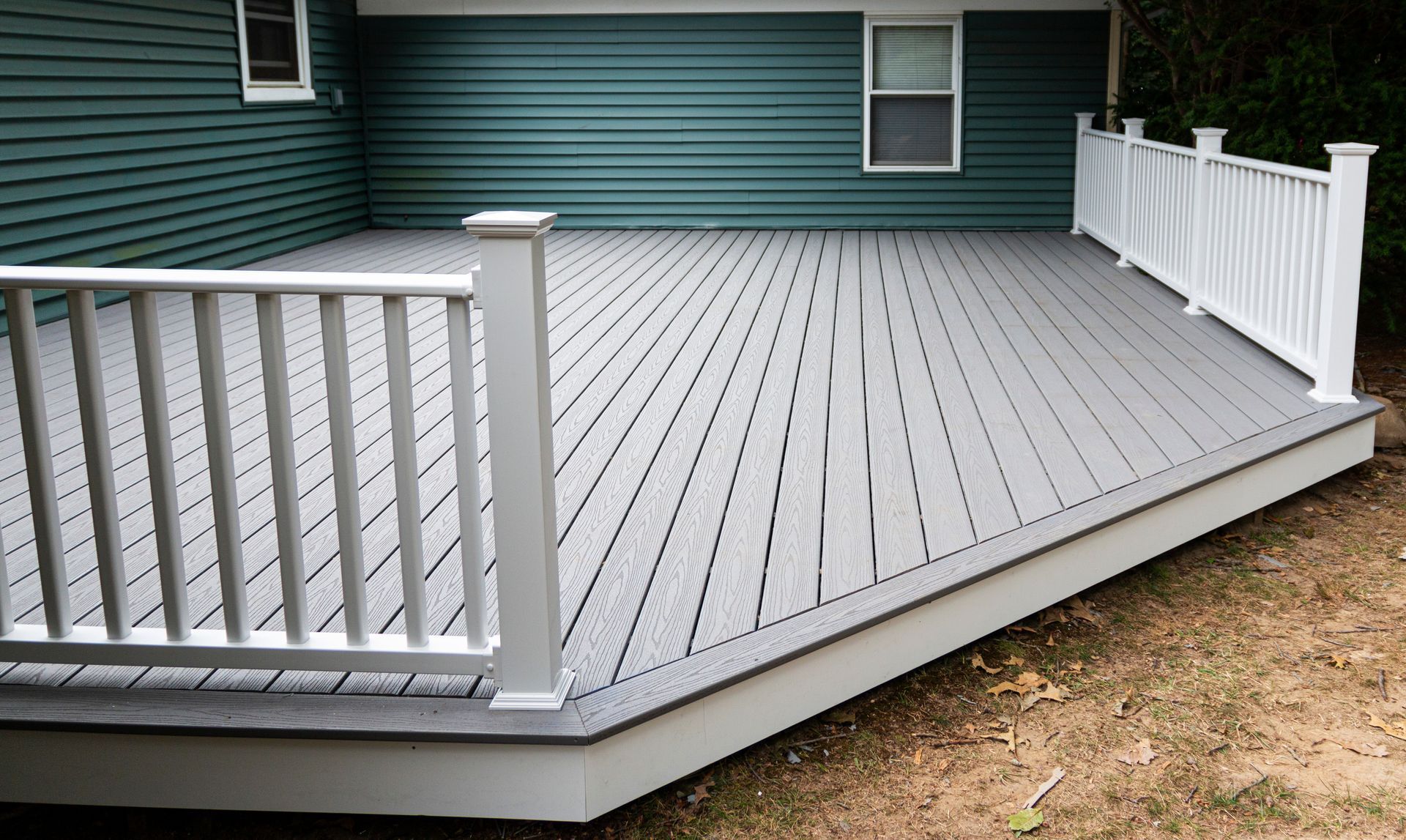Gray composite deck with white railing against a teal house exterior, surrounded by grass.