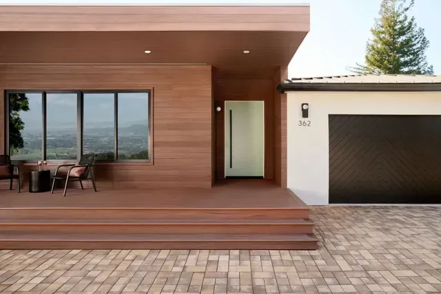 Modern home exterior with brown wood siding, porch, and a black garage door.