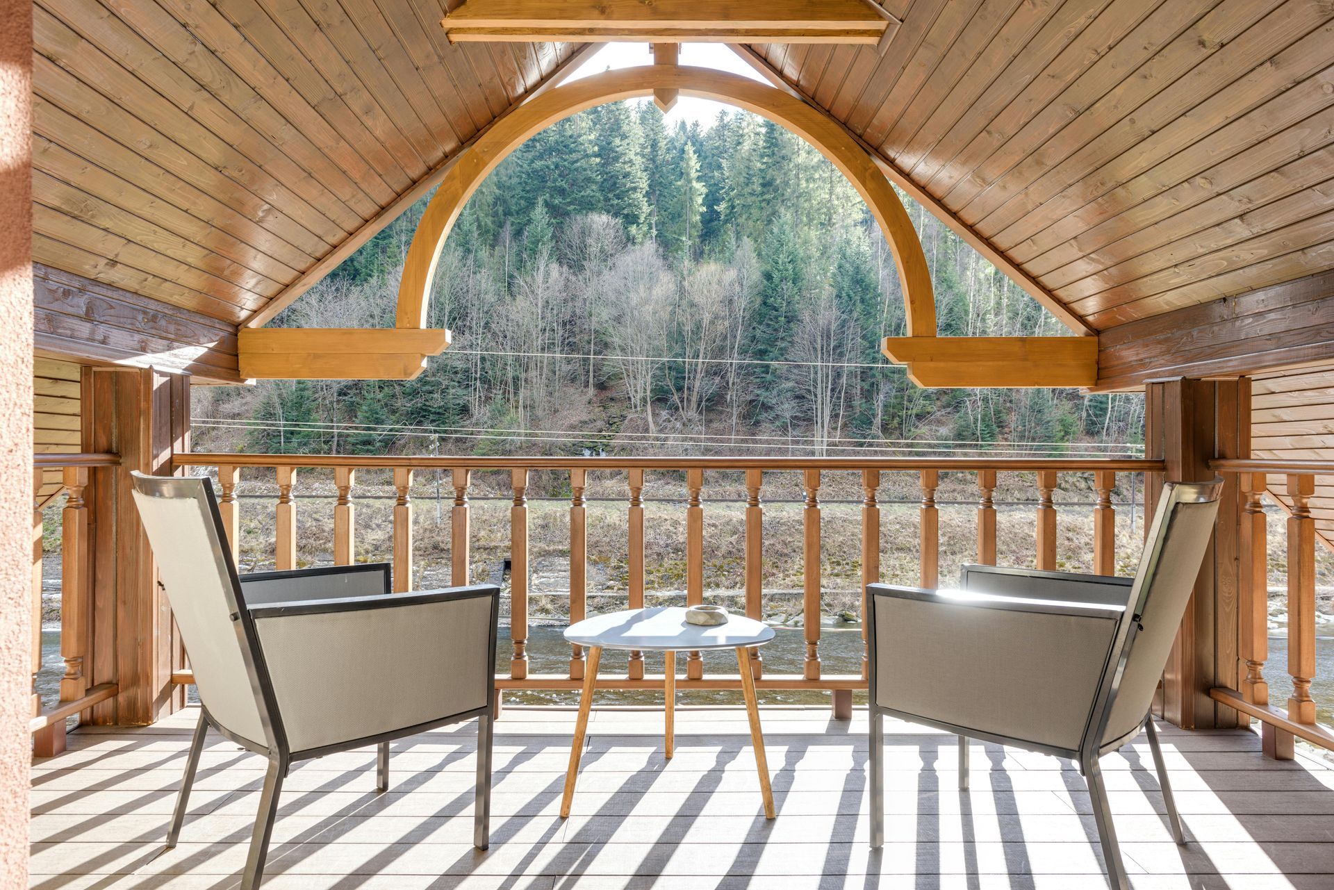 Two chairs and a small table on a wooden porch, overlooking a forest.