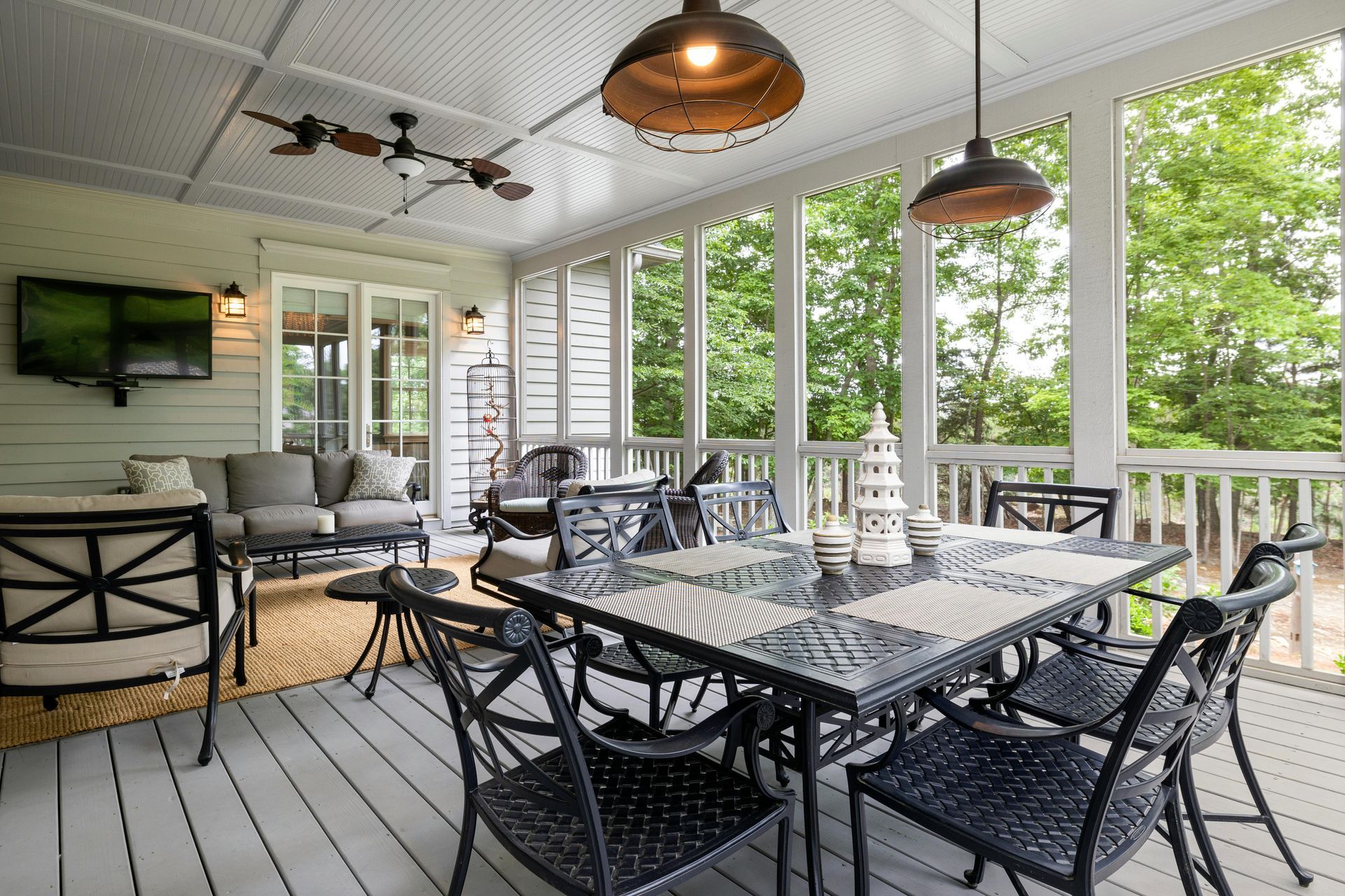 Screened porch with dining table, seating area, ceiling fans, and outdoor views.