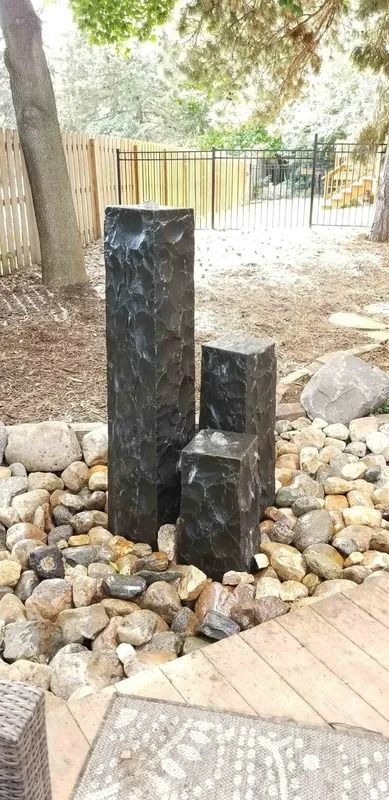 Black stone water feature in a pebble garden beside a wooden deck and trees