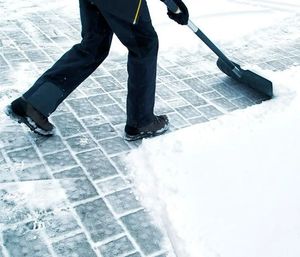 Person shoveling snow from a paved walkway with a black snow shove