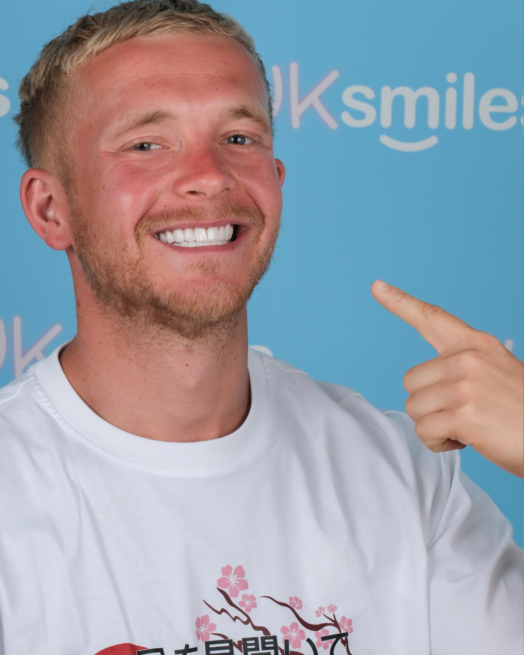Man with new white teeth smiles, hand points. Blue background with 