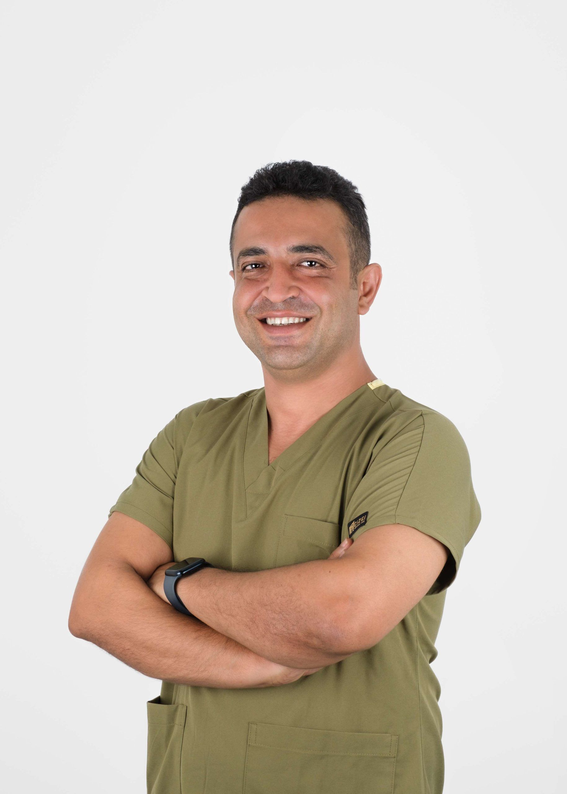 Man in olive scrubs with arms crossed, smiling.