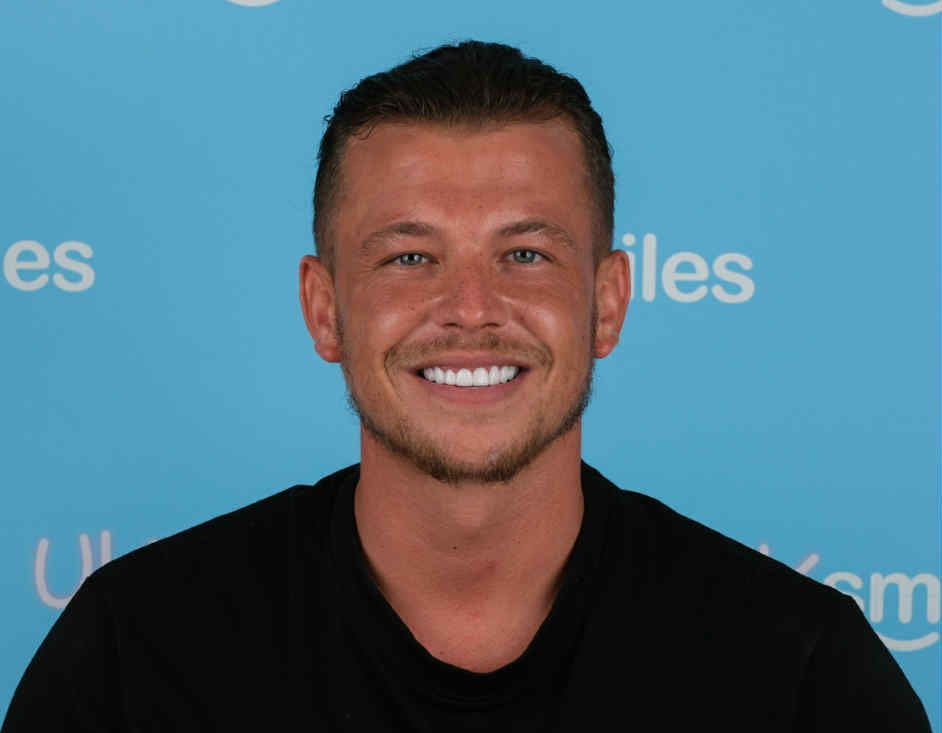 Man with a bright smile wearing a black shirt, against a blue background.