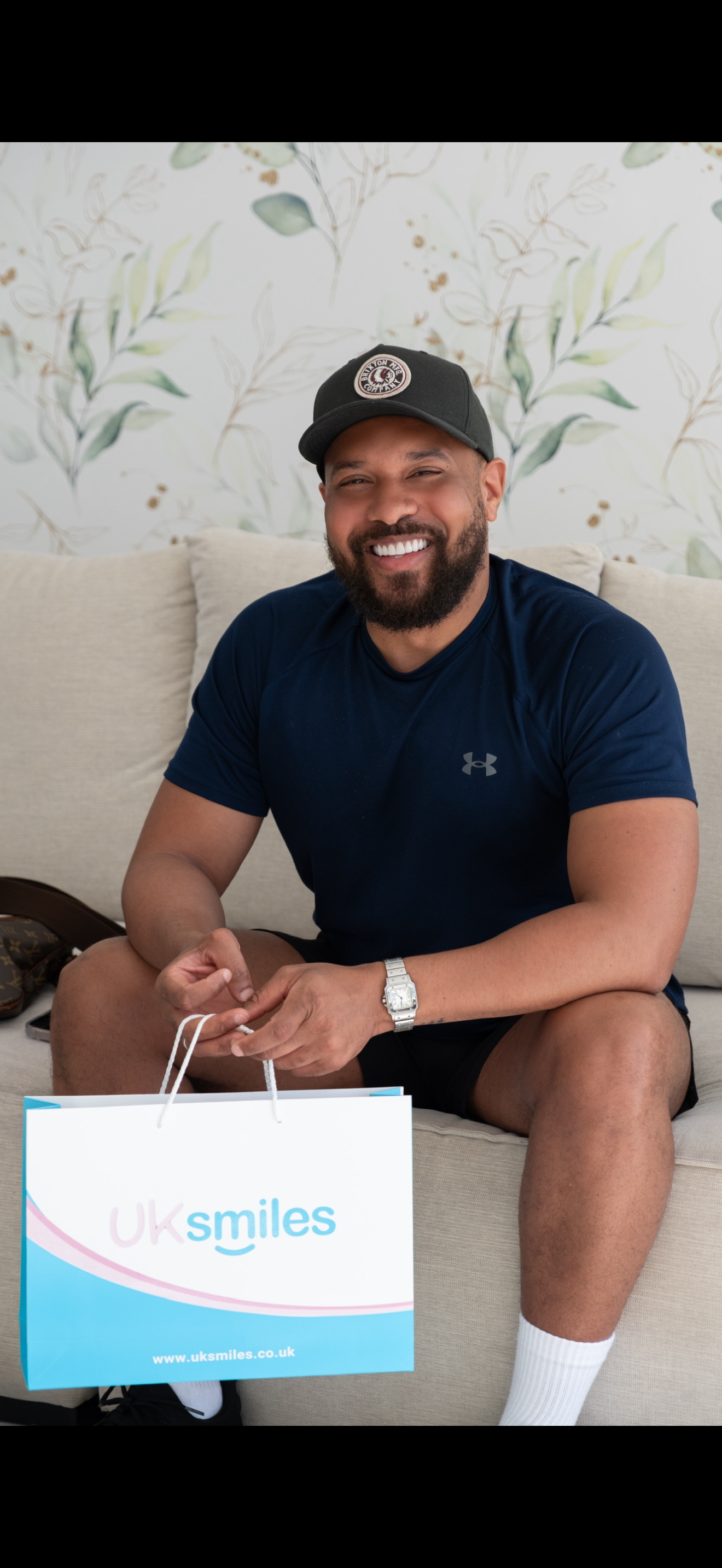Man in a baseball cap smiles, holding a