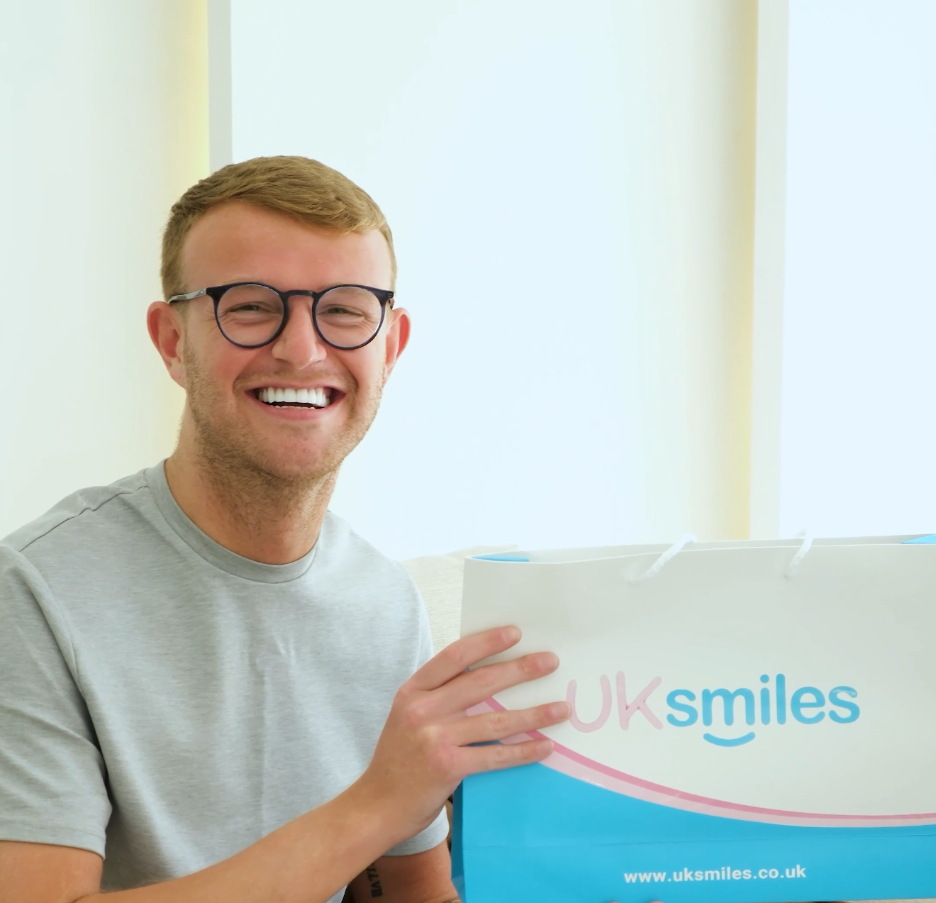 Man with glasses smiles, holding a box of UK smiles teeth whitening kit.