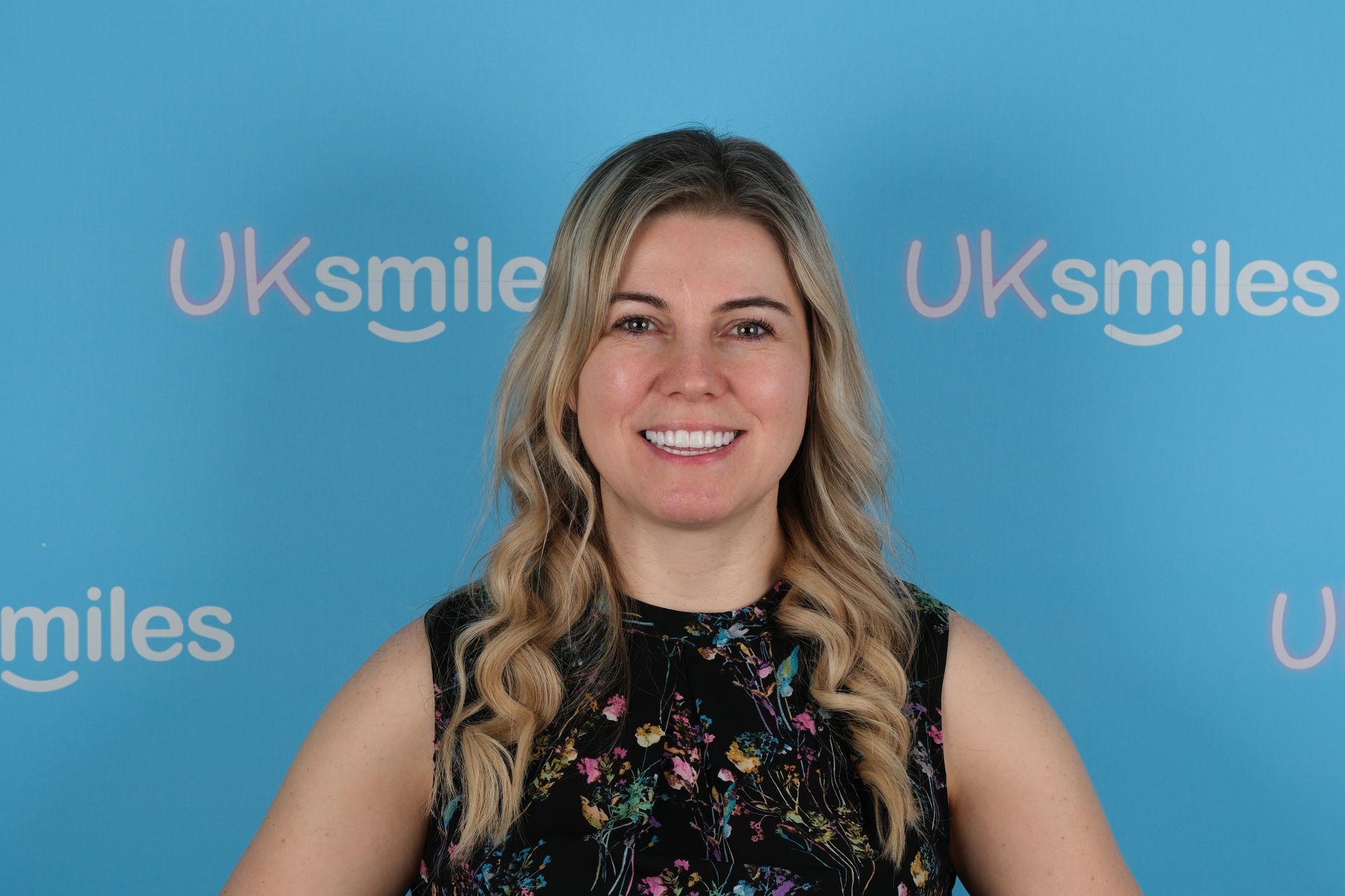 Woman with blonde hair smiling, in front of a blue backdrop with the