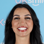 Woman with dark hair and large smile, white teeth, against a light blue backdrop.