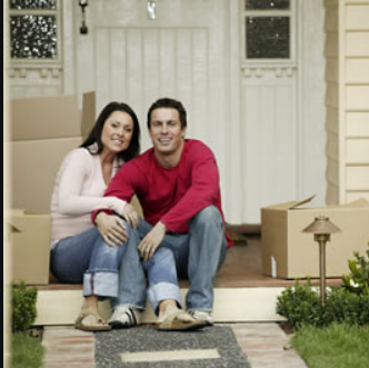 Couple sitting on front steps beside moving boxes, smiling outside a house