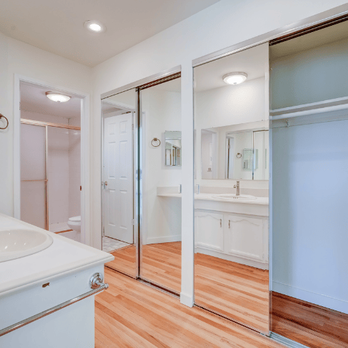 Bright bathroom with dual mirrors, white vanity, glass shower, and hardwood floors.