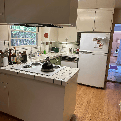 Cozy kitchen with white cabinets, tiled island, stove, fridge, and hardwood floor.